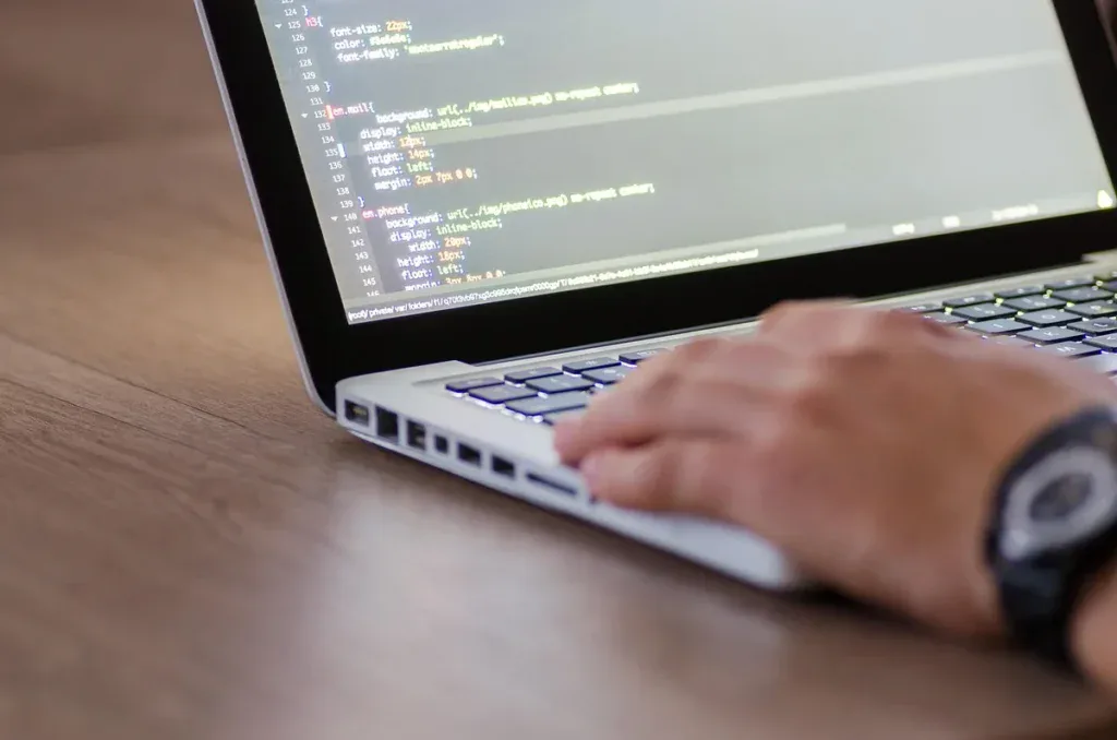 Dłonie na klawiaturze laptopa z kodem na ekranie
