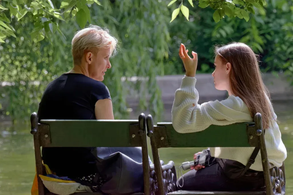 Matka i nastoletnia córka rozmawiają na ławce nad wodą, gdy nastolatek nie chce rozmawiać
